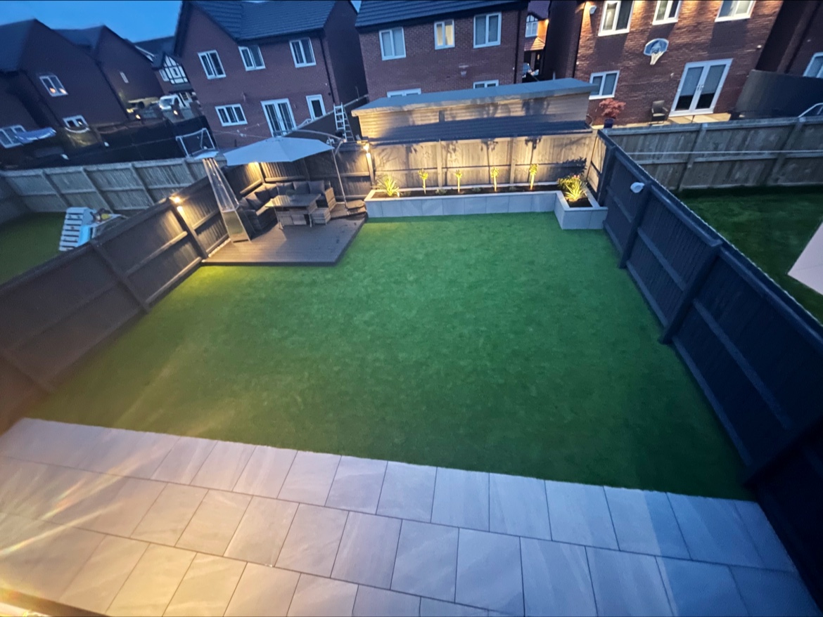 Porcelain patio, artificial lawn and lit decking seating area at dusk