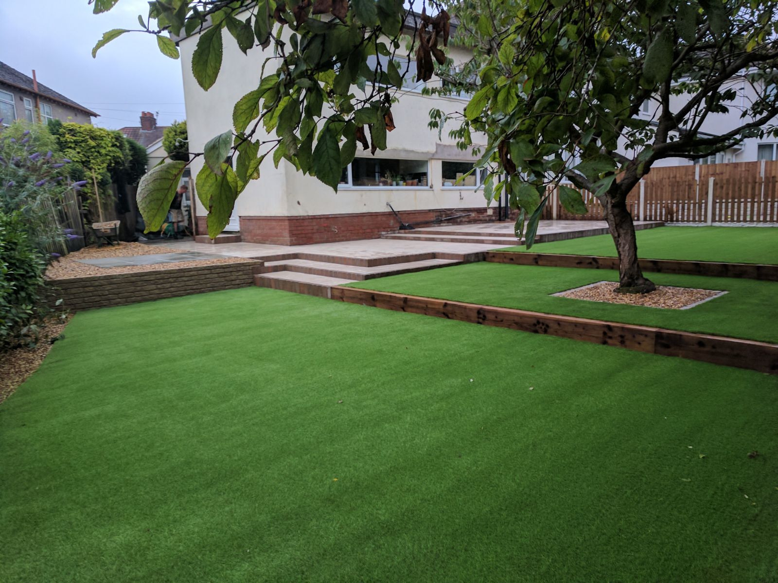 Tiered artificial lawn with timber sleeper edging and wide patio steps behind a family home