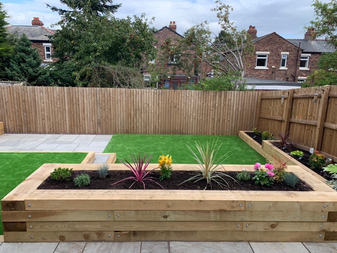 Oak sleeper raised beds with fresh planting beside a grey patio