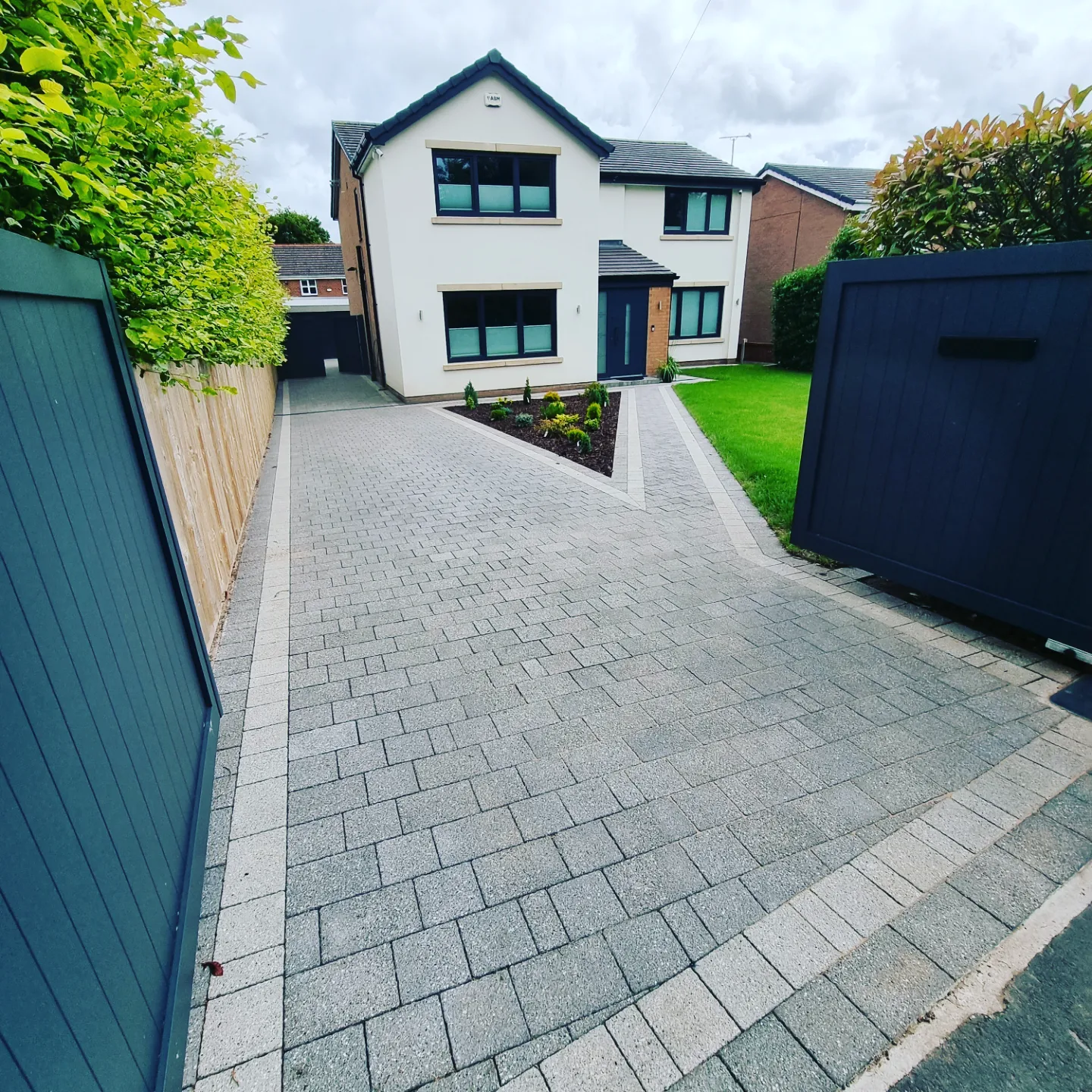 Block-paved driveway with a triangular planted bed leading to a detached house