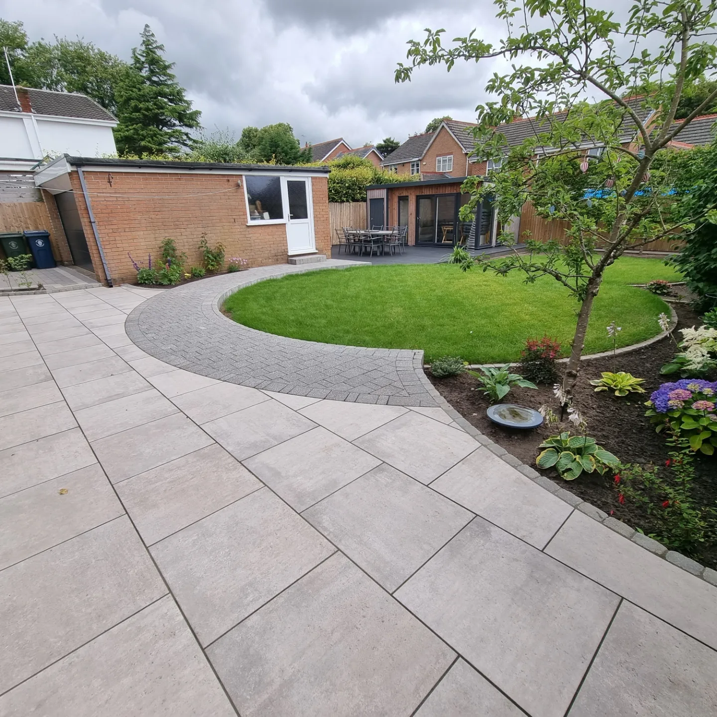 Light porcelain patio with a curved block-paved path around a circular lawn