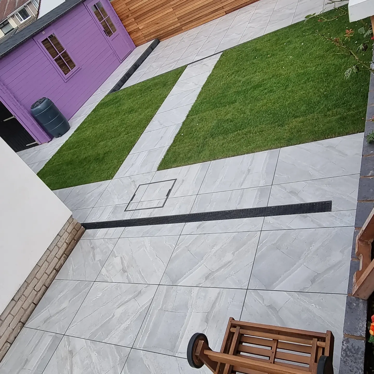 Grey porcelain patio with slot drain and lawn panels divided by a porcelain path